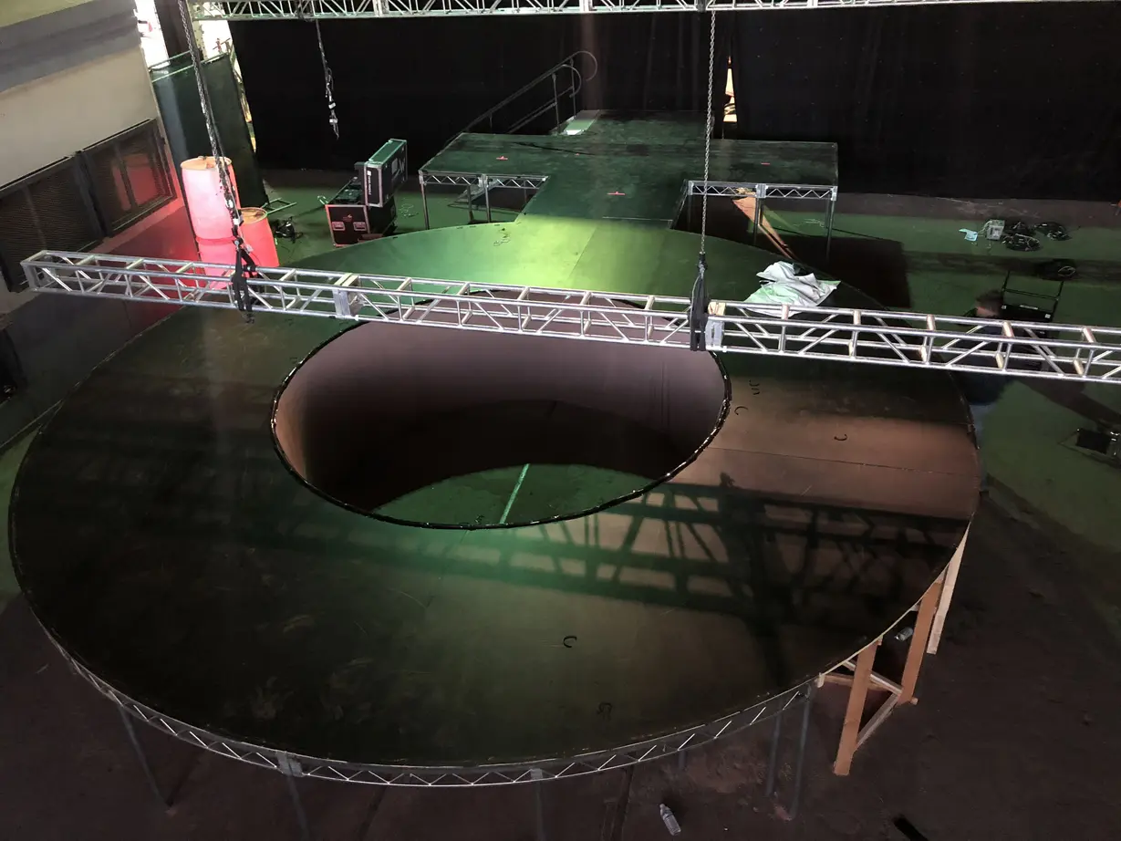 Circular and Round Stage Rental — Round black stage with crescent cutout under flown truss — in-the-round build pre-show