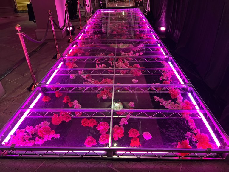 Customized Stages and Fabrication — LED-lit acrylic runway with florals under clear deck panels — immersive fashion entrance build