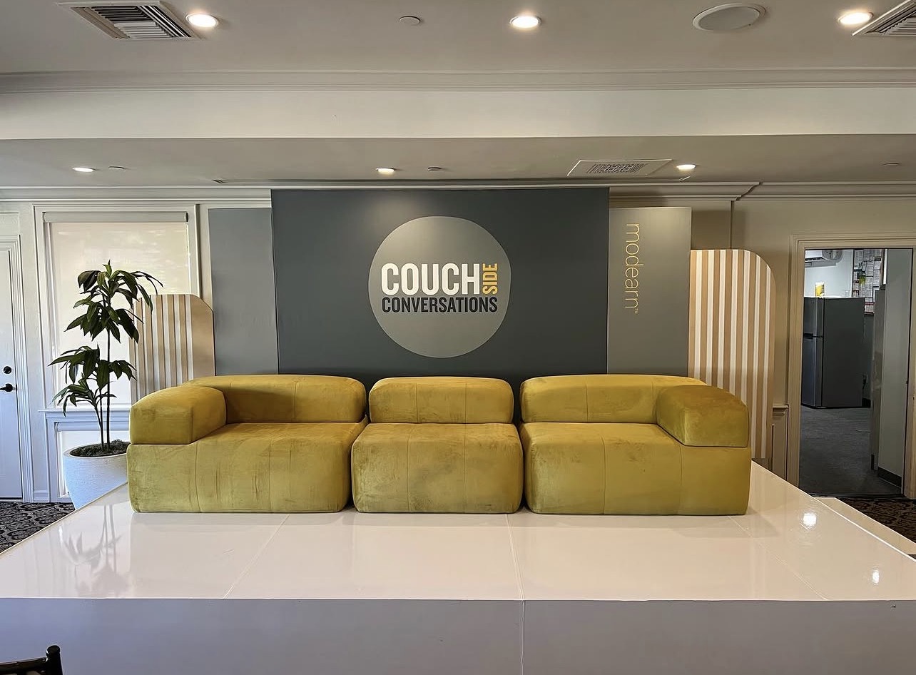 Custom Couchside Conversations backdrop with side modearn brand panel and white riser stage — modular yellow lounge build