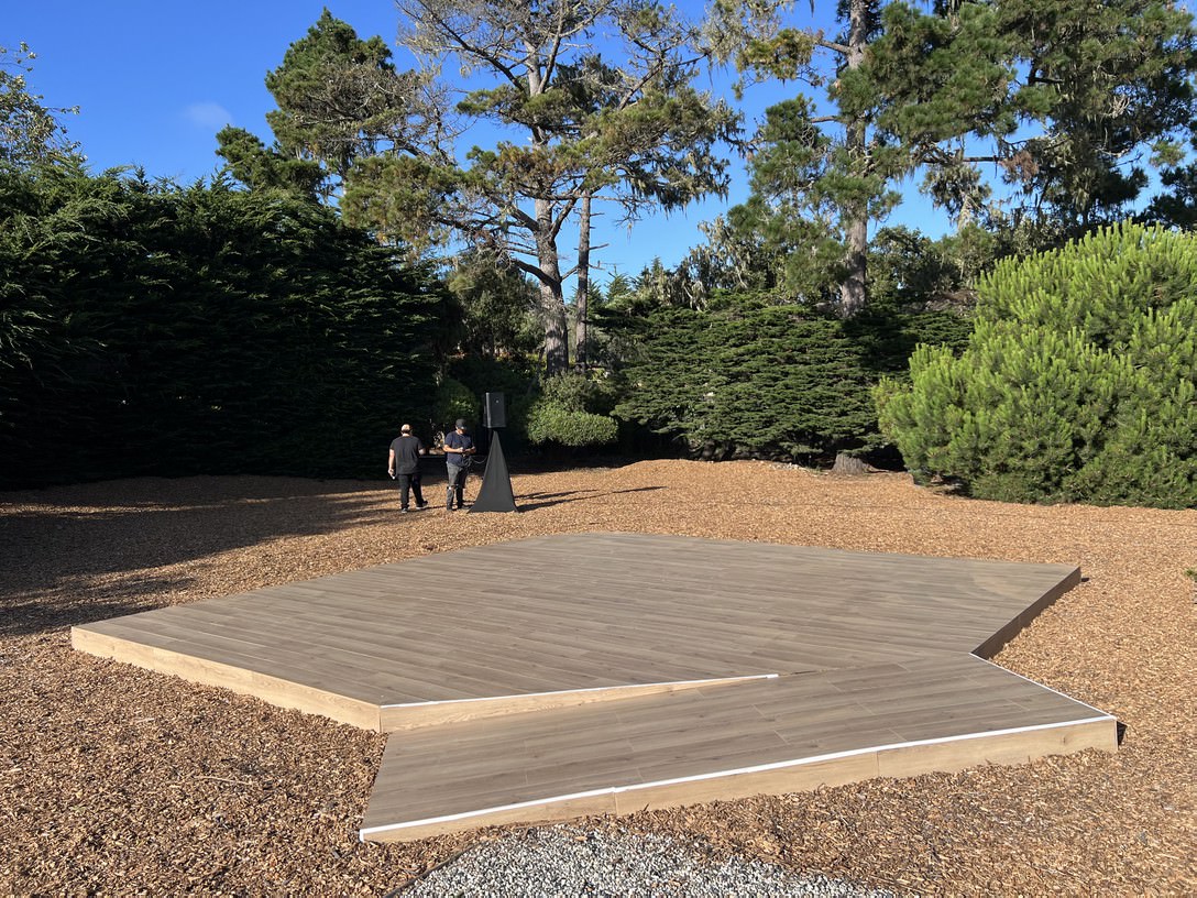Temporary Sub Floor Rental — Wood-finish square stage with corner step on mulch — outdoor garden over-grade install